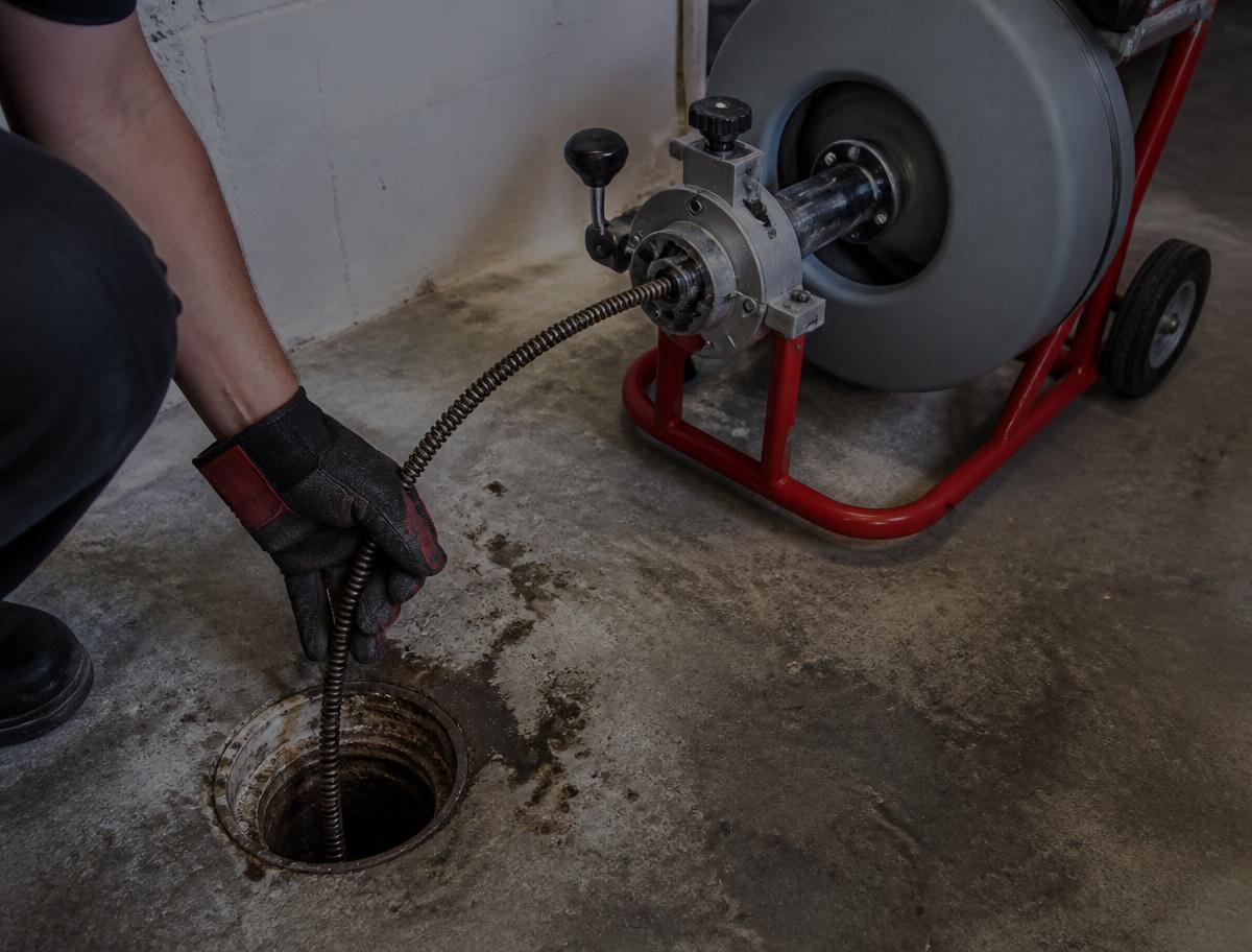 Motorized drain auger cable being fed into a basement floor drain during a drain cleaning service