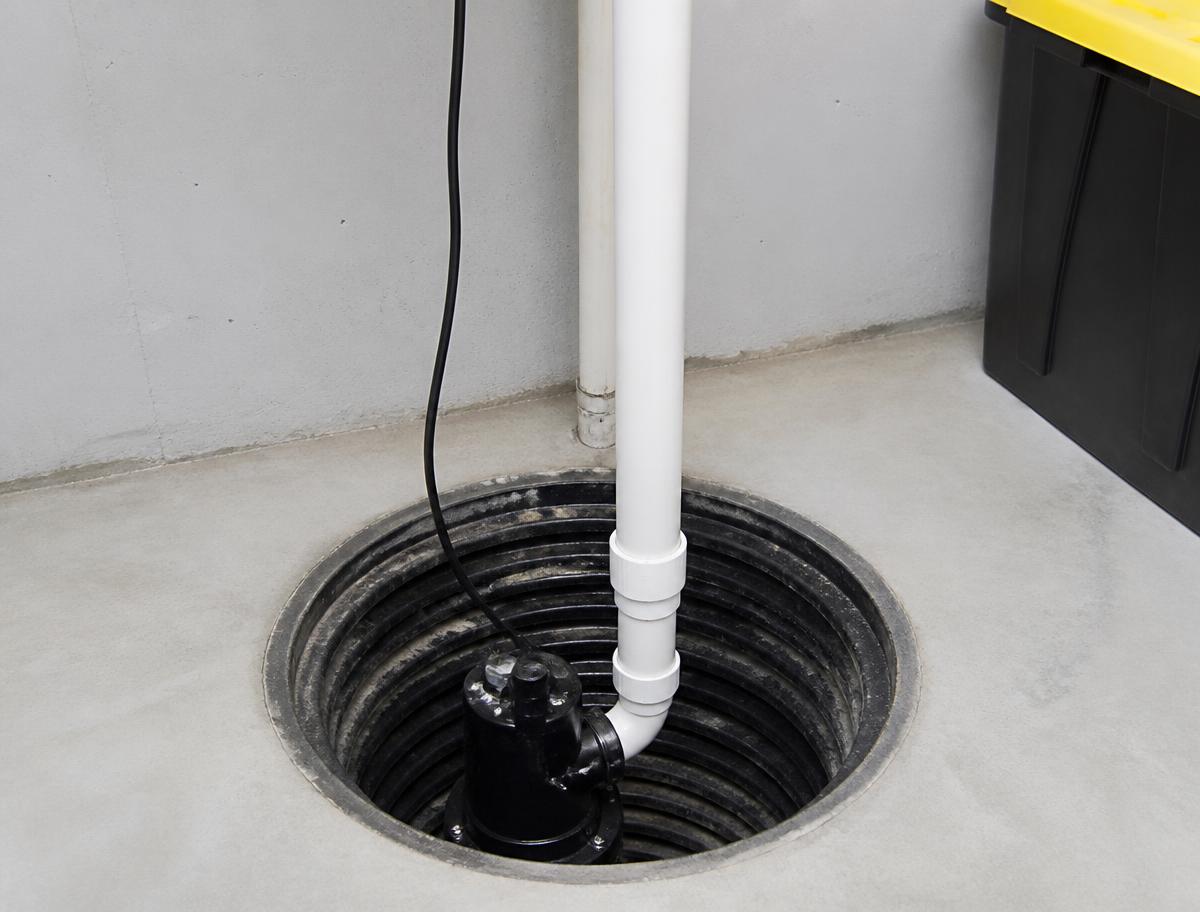 Sump pump seated in a basement sump pit with white PVC discharge piping